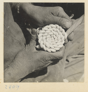Woman forming a spiral braid of twisted husks to make a maize straw cushion