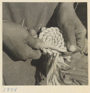 Woman forming a spiral braid of twisted husks to make a maize straw cushion