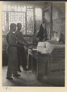 Two men heating glass in an oven in a glassblowing workshop