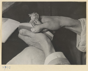 Man smoothing rough edges of a wooden comb with a string of glass beads in a workshop