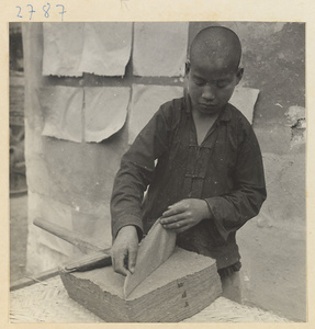 Boy hanging sheets of paper on a wall to dry outside paper-making shop