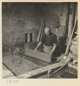 Man lifting a screen covered with paper pulp out of a vat in a paper-making shop