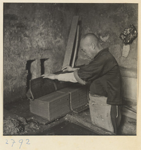 Man placing a screen covered with paper pulp on a stack of screens in a paper-making shop