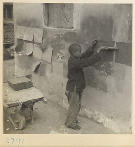 Boy hanging sheets of paper on a wall to dry outside paper-making shop