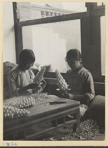 Two women assembling glass balls into bunches of artificial grapes in a workshop