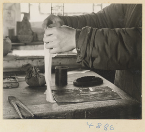 Man laying a piece of cloth or paper on a metal sheet coated with soot in a workshop that makes iron pictures