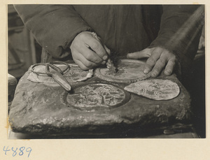 Man impressing a relief pattern onto a metal sheet in a workshop that makes iron pictures