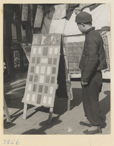 Man looking at a street vendor's display stand in front of a seal-carving shop during New Year's.