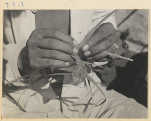 Street vendor braiding reeds to make a toy