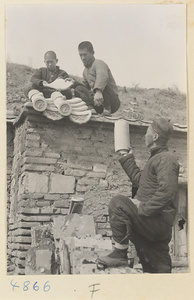 Men demonstrating how roof tiles fit together on the roof of a tile and brick factory near Mentougou Qu