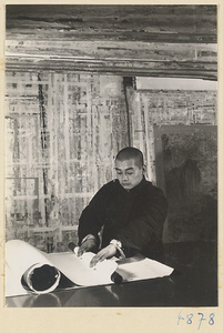 Man in a scroll-mounting shop attaching the bottom roller bar called a zhou to a scroll painting