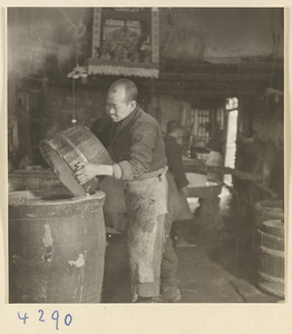 Man emptying a bucket of bean curds into a vat in a tofu-making shop