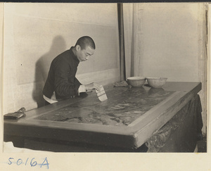 Interior of a scroll-mounting shop showing a man smoothing away air bubbles with a soft brush called a shui shua