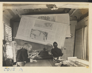 Interior of a scroll-mounting shop showing mounters working on the back of a scroll painting and moving a drying board called a Zhuang ban