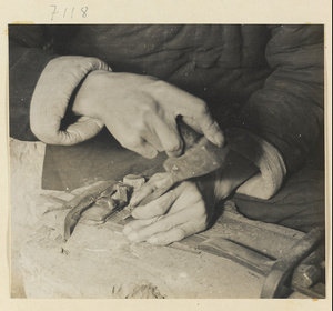 Man tooling designs into a piece of metal in a blacksmith's shop