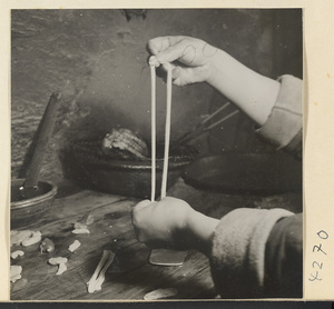 Kitchen interior showing a man stretching dough to make oil cakes