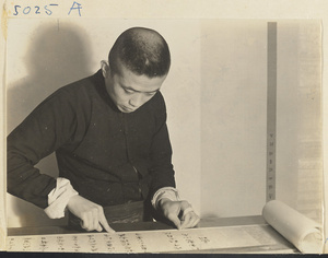 Interior of a scroll-mounting shop showing a man adhering paper strips to the edge of a scroll