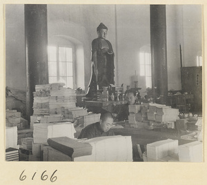 Monks at work in the bindery of a Buddhist temple with altar and statue of Buddha in background