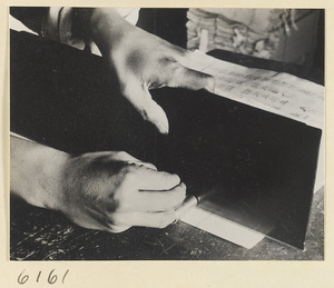 Monk preparing a stack of printed sheets for binding in the bindery of a Buddhist temple