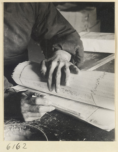 Monk gluing printed sheets together in the bindery of a Buddhist temple