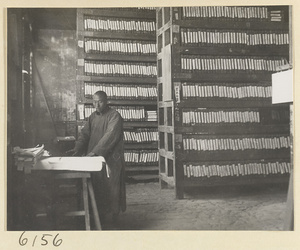 Monk preparing a new edition of a sutra in the printing room of a Buddhist temple with shelves of printing blocks in the background