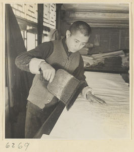 Interior of a scroll-mounting shop showing a man brushing a backed scroll painting with a stiff brush called a zhong pi shua