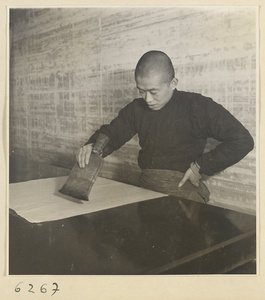 Interior of a scroll-mounting shop showing a man brushing a backed scroll painting with a stiff brush called a zhong pi shua