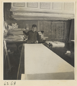 Interior of a scroll-mounting shop showing a man brushing a backed scroll painting with a stiff brush called a zhong pi shua