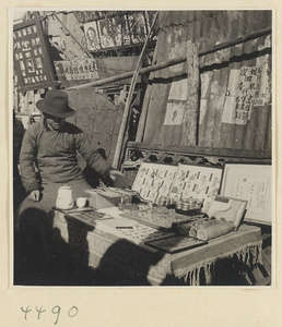 Street doctor reaching for a snake at his stand displaying medicines and posters picturing ailments