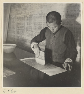 Interior of a scroll-mounting shop showing a man moistening a scroll painting with a soft brush on a mounting table called a da an