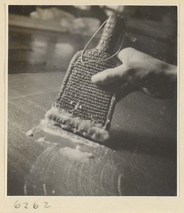 Interior of a scroll-mounting shop showing a man applying paste onto the back of a scroll painting with a brush