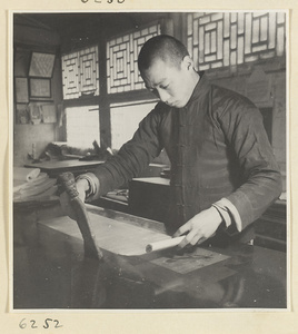 Interior of a scroll-mounting shop showing a man adhering a backing to a scroll by softly tapping with a stff brush called a zong pi shua