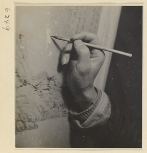 Interior of a scroll-mounting shop showing a man touching up areas of loss on a scroll painting as it hangs on a drying board called a zhuang ban