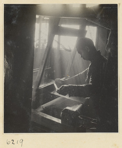 Interior of copper-net factory showing a man working at a loom