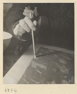 Interior of a scroll-mounting shop showing a man treating the back of a scroll painting with a soft brush