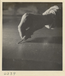 Interior of a scroll-mounting shop showing a man using iron tweezers to remove bits of paper from the back of a scroll painting