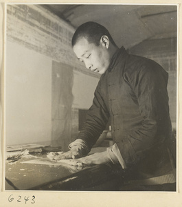 Interior of a scroll-mounting shop showing a man removing the old backing from a scroll