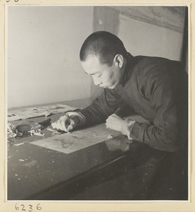 Interior of a scroll-mounting shop showing a man removing the old backing from a scroll painting