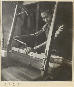 Interior of copper-net factory showing a man working at a loom