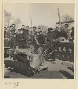 Patent medicine seller of body-building ointments flexing a bow with his teeth in front of a crowd at Tianqiao Market