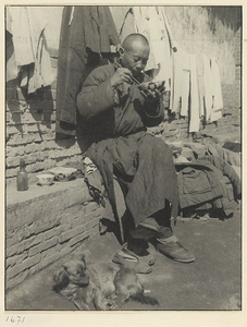 Second-hand clothes vendor with a dog at his feet sitting and eating next to a display of his wares
