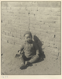 Child dressed in winter clothes seated in the street