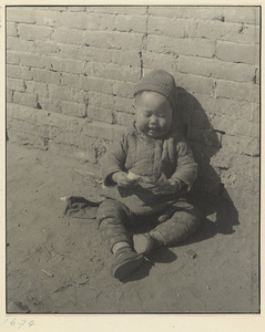 Child dressed in winter clothes seated in the street