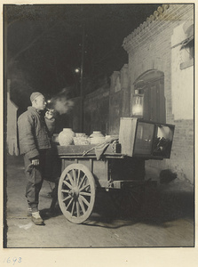 Food vendor smoking a pipe and selling refreshments from a cart at night