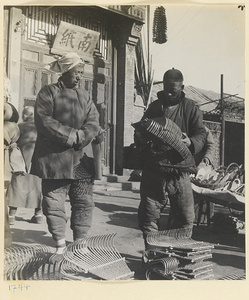 Vendor selling rake heads to a customer outside a shop with shop signs