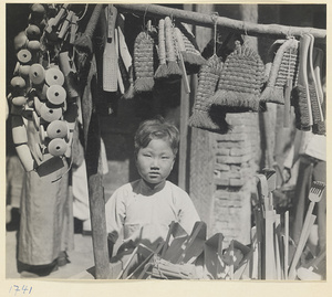 Child next to a vendor's stand displaying brushes and wooden household goods
