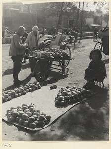 Street vendors displaying their wares on a cart and a mat selling produce to a rickshaw puller