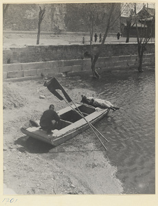 Two men on a boat beached by a city moat