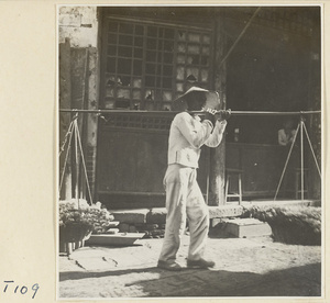 Man carrying a shoulder pole with baskets of produce on a street in Tai'an