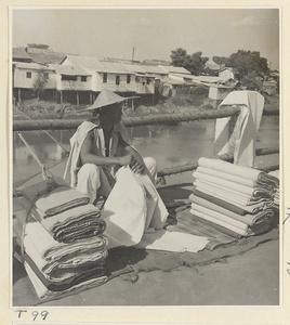 Man selling cloth by the river at Tai'an with houses on stilts in the background